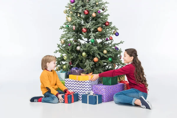 Lächelnde Geschwister am Weihnachtsbaum mit Geschenken auf Weiß — Stockfoto