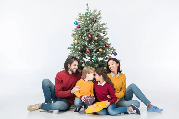 Niños felices con regalos con padres sentados cerca del árbol de Navidad aislados en blanco - foto de stock