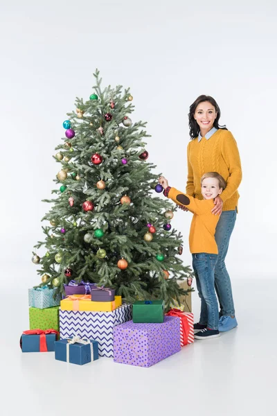 Lächelnde Mutter mit Sohn schmückt Weihnachtsbaum mit Geschenken auf Weiß — Stockfoto