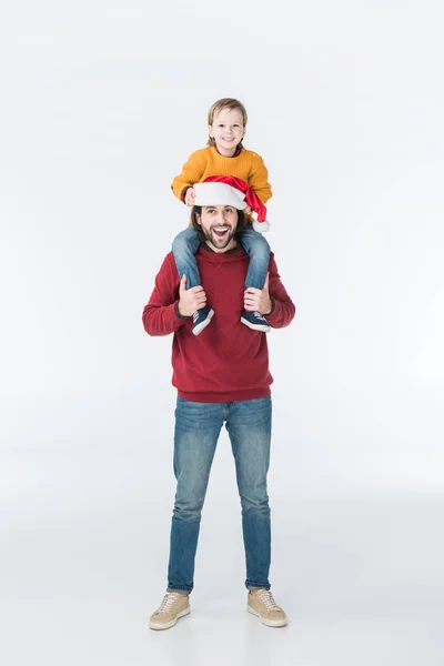 Glücklicher Vater mit Weihnachtsmütze, der Sohn auf den Schultern isoliert auf weißem Grund trägt — Stockfoto