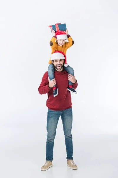 Padre en sombrero de santa llevar hijo con navidad presente en los hombros aislados en blanco - foto de stock