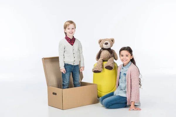 Niño de pie en una caja de cartón listo para mudarse con su hermana a una nueva casa aislada en blanco - foto de stock