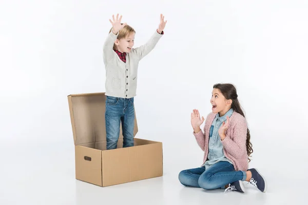 Удивленный парень с мальчиком, стоящим в картонной коробке, изолированной на белом — стоковое фото