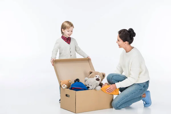 Happy mother with son sitting near cardboard box with toys isolated on white — Stock Photo