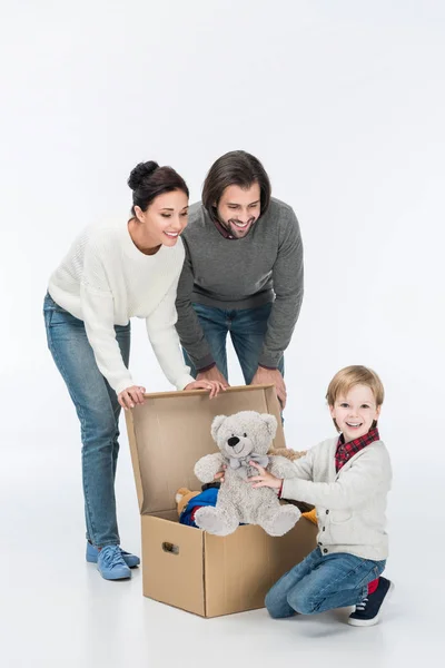 Parents heureux avec fils tenant ours en peluche et assis près de la boîte en carton avec des jouets isolés sur blanc — Photo de stock