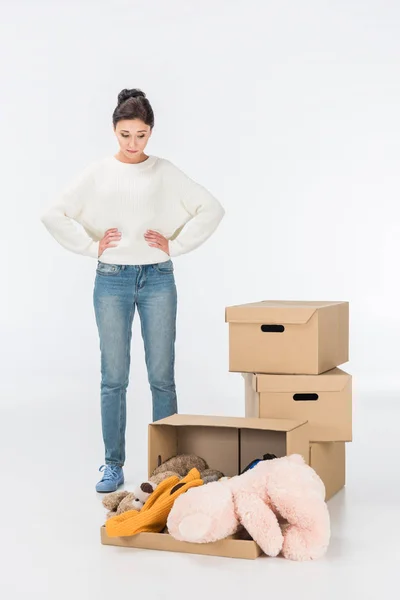 Femme réfléchie regardant boîte en carton avec des jouets isolés sur blanc — Photo de stock