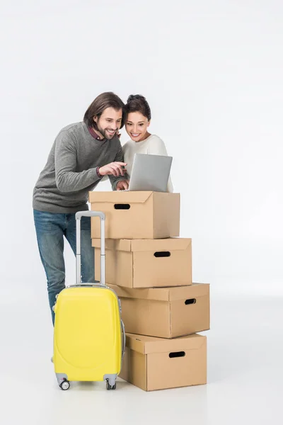 Smiling couple using laptop on cardboard boxes isolated on white — Stock Photo