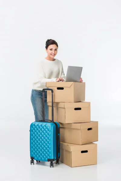 Femme souriante utilisant un ordinateur portable sur des boîtes en carton isolées sur blanc — Photo de stock