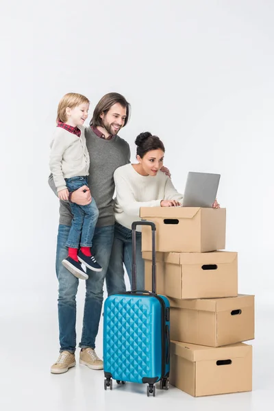 Famille heureuse en utilisant un ordinateur portable sur des boîtes en carton isolé sur blanc — Photo de stock