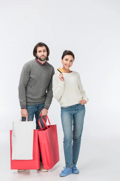 Вдумчивый мужчина с сумками для покупок и улыбающаяся женщина, показывающая кредитную карту изолированы на белом — стоковое фото