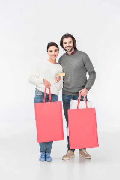 Sonriente pareja con bolsas de compras y mujer mostrando tarjeta de crédito aislada en blanco - foto de stock