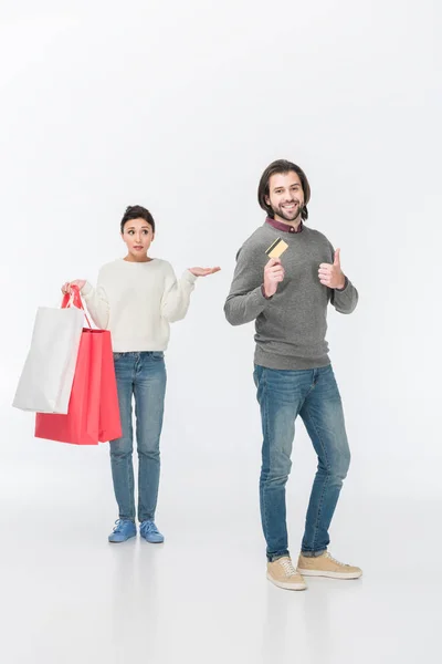 Mujer con bolsas de compras mientras que el hombre muestra el pulgar hacia arriba y la tarjeta de crédito aislado en blanco - foto de stock