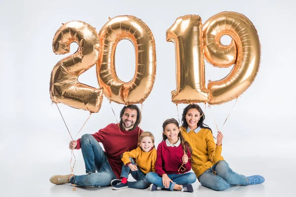 Feliz familia sosteniendo signo 2019 hecho de globos de oro para el nuevo año aislado sobre fondo blanco - foto de stock