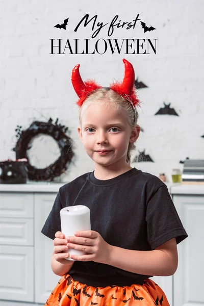 Ritratto di un bambino con le corna rosse del diavolo che tiene la candela in mano a casa, con la scritta 