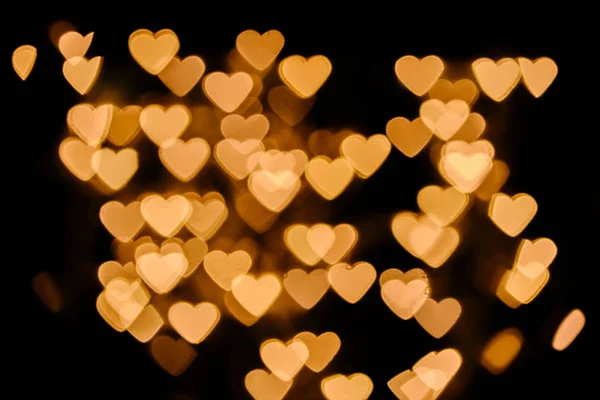 Corações dourados bokeh luzes no fundo preto — Fotografia de Stock