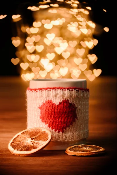 Close up view of cup of hot drink and dry orange pieces on wooden tabletop with hearts bokeh lights background — Stock Photo