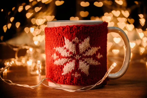 Vue rapprochée de tasse de boisson chaude et guirlande sur table en bois avec des cœurs bokeh lumières fond — Photo de stock