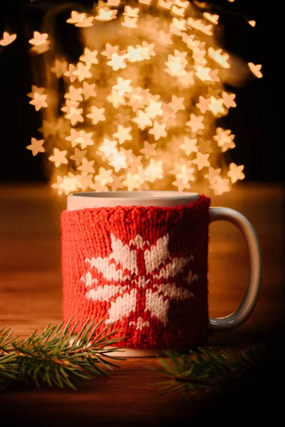 Close up view of cup of hot drink and pine tree branches on wooden tabletop with stars bokeh lights background — Stock Photo