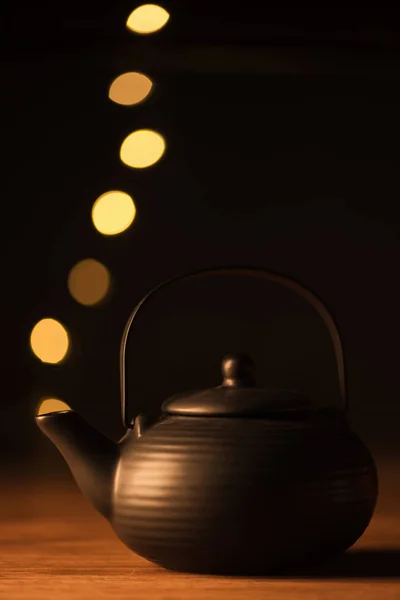 Close up view of clay teapot and golden bokeh lights as steam on black background — Stock Photo