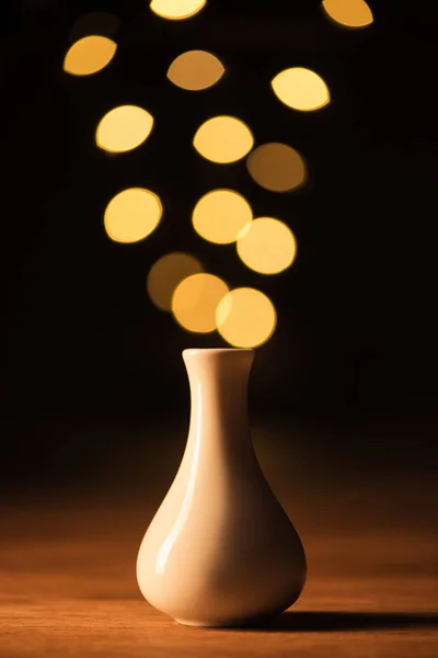 Close up view of white vase and yellow bokeh lights on black background — Stock Photo