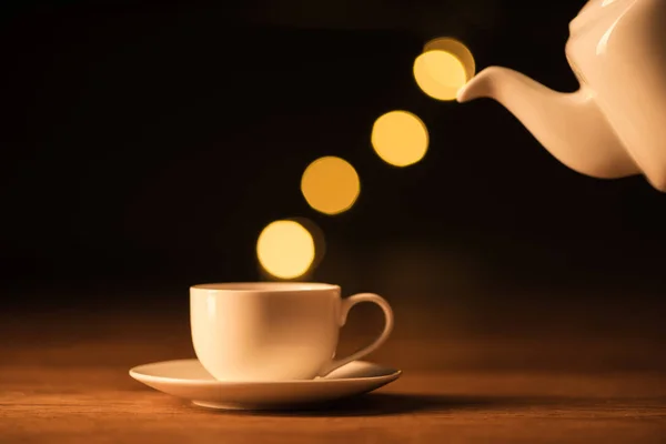 Vista de perto do bule branco, xícara de café e bokeh luzes no fundo preto — Fotografia de Stock