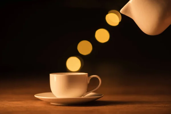 Vista de perto do jarro branco, xícara de café e bokeh luzes no fundo preto — Fotografia de Stock