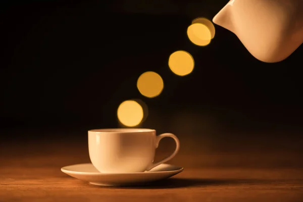 Vista de cerca de la jarra blanca, taza de café y luces bokeh en el fondo negro — Stock Photo