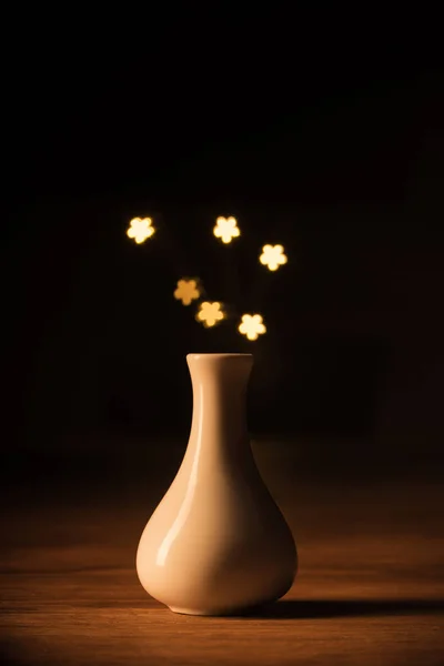 Vista de perto do vaso branco e estrelas amarelas bokeh luzes no fundo preto — Fotografia de Stock