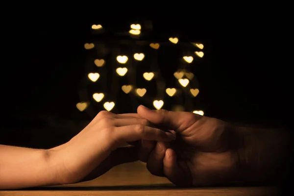 Cropped shot of couple holding hands with hearts bokeh background — Stock Photo