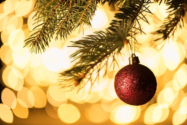Vue rapprochée de boule de Noël rouge suspendue sur un pin avec des lumières bokeh arrière-plan — Photo de stock