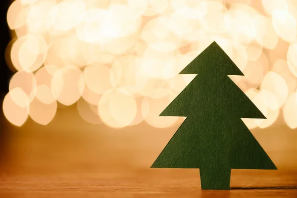 Close up view of green paper christmas tree on wooden tabletop and bokeh lights background with copy space — Stock Photo