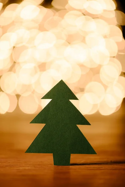 Close up view of green paper christmas tree on wooden tabletop and bokeh lights background — Stock Photo