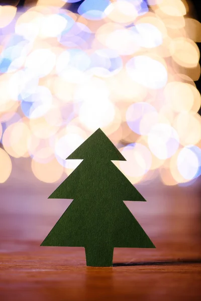 Nahaufnahme von grünem Papier Weihnachtsbaum auf hölzerner Tischplatte und Bokeh Lichter Hintergrund — Stockfoto