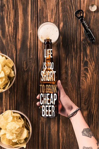 Cropped image of woman pouring beer into glass at wooden table with crispy chips, with 