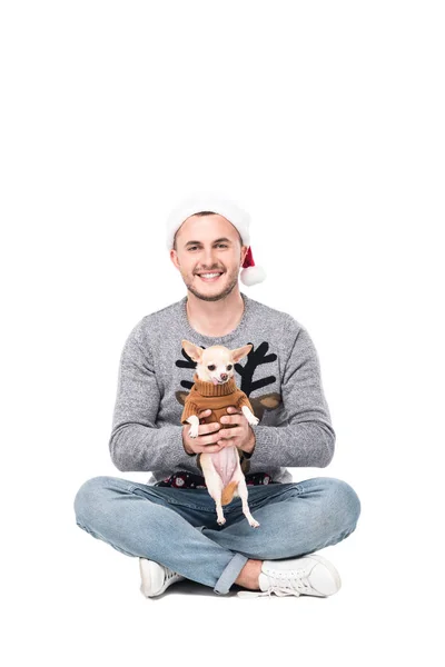 Joven en santa claus sombrero celebración chihuahua perro en suéter aislado en blanco - foto de stock