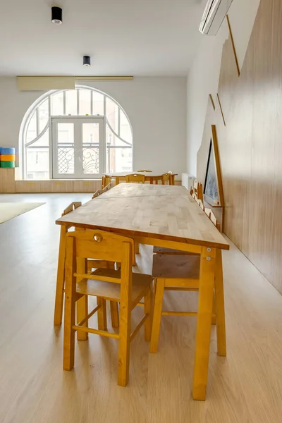 Mesas de madera y sillas pequeñas en el interior del aula de jardín de infantes moderno - foto de stock