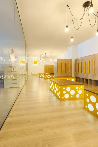 Wooden lockers, benches and mirror in modern illuminated kindergarten cloakroom — Stock Photo