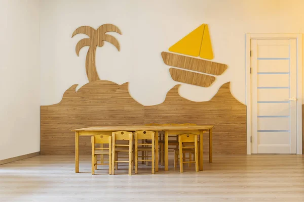 Уютная комната с деревянным столом и стульями и декоративными элементами в стене в современном детском саду — стоковое фото