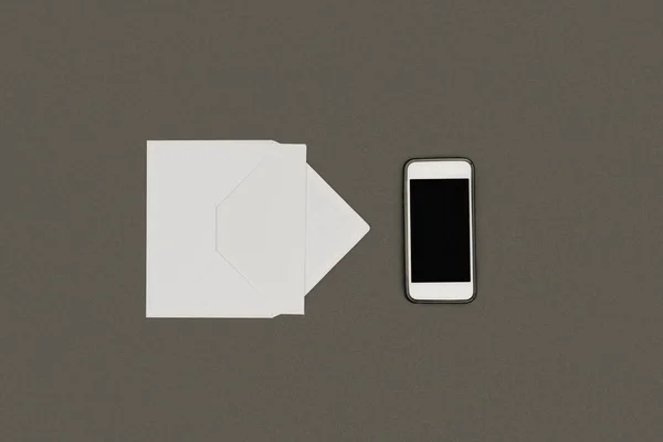 Вид зверху на білий конверт, порожню карту і смартфон з порожнім екраном ізольовано на сірому — стокове фото