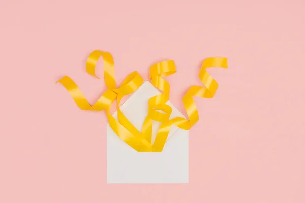 Close-up view of open white envelope with yellow ribbons isolated on pink — Stock Photo