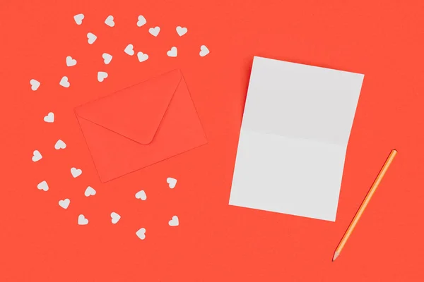 Top view of blank white card, pencil, red envelope and small hearts isolated on red — Stock Photo