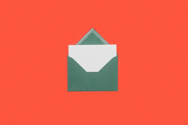 Close-up view of green envelope with white card isolated on red — Stock Photo