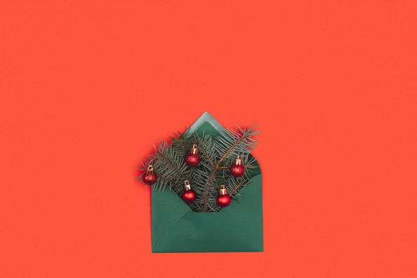 Close-up view of green envelope with fir twigs and shiny christmas baubles isolated on red — Stock Photo