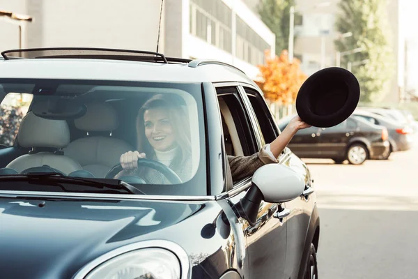 Selektiver Fokus einer fröhlichen Frau, die sich im Auto an der Stadtstraße mit schwarzem Hut auslehnt — Stockfoto
