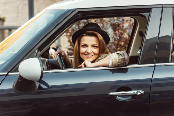 Porträt einer glücklichen, stylischen Frau mit schwarzem Hut, die in einem Auto auf einer städtischen Straße sitzt — Stockfoto
