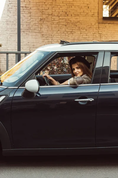 Mujer adulta en chaqueta a cuadros y sombrero negro sentado en el coche en la calle urbana - foto de stock