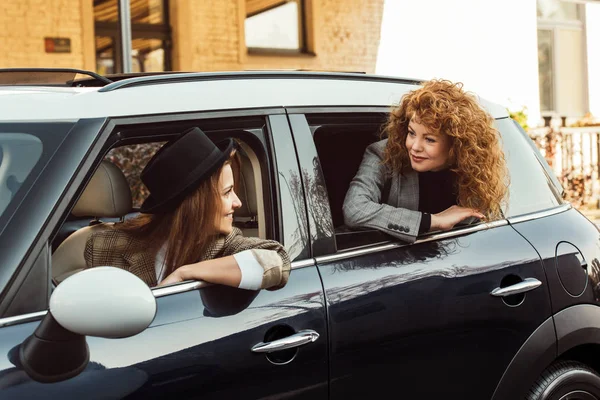 Happy female friends leaning out from car and looking at each other — Stock Photo