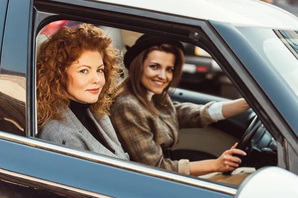 Attractive happy woman in black hat driving car while her ginger female friend sitting near — Stock Photo