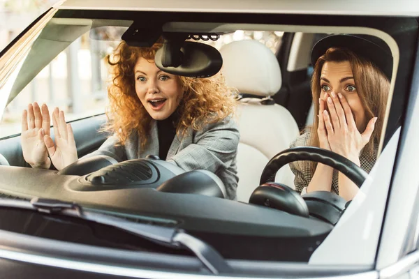 Surprised adult female friends gesturing by hands and sitting in car — Stock Photo
