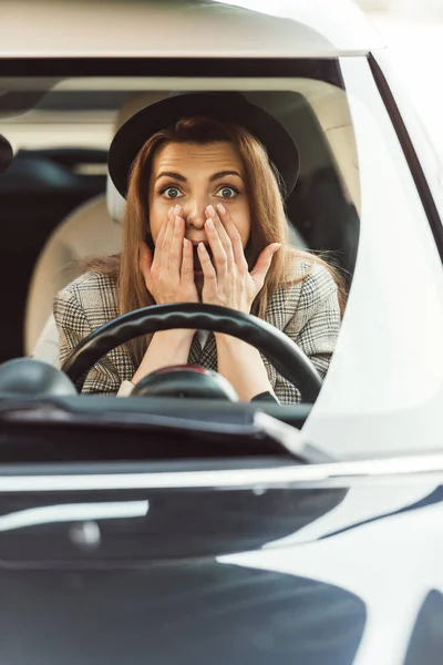 Шокована жінка жестикулює руками, сидячи на кермі в машині — стокове фото
